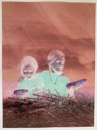 Zwei Kinder sitzen auf einem Feld und halten Maiskolben in der Hand. Ein Kind hat den Arm um das andere gelegt. Das Bild zeigt invertierte, negative Farben.
