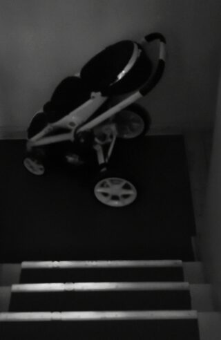 Ein Kinderwagen steht in einer schwach beleuchteten Umgebung oben auf einer Treppe.