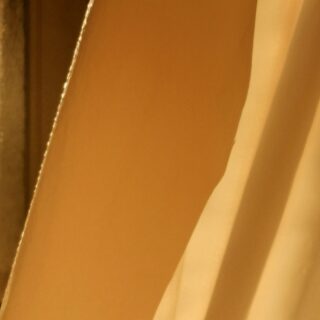 Nahaufnahme von hellbraunen und beigen Oberflächen mit glatten Texturen und sanfter Beleuchtung, möglicherweise Stoff oder Papier, wodurch eine abstrakte Komposition entsteht.