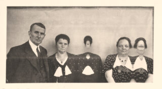 Ein altes Foto von einem Mann und drei Frauen, wobei die Gesichter zweier Frauen verzerrt sind oder fehlen, die vor einem schlichten Hintergrund stehen.