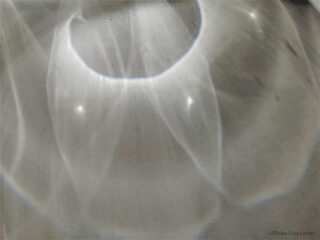 Abstraktes Muster aus Licht und Schatten mit geschwungenen, durchscheinenden Formen und weichen Farbverläufen auf einer blassen Oberfläche. ©Élodie Cruz Laufer.