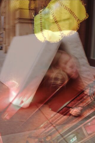 Eine verschwommene Person liegt teilweise unter einer umgekippten Matratze auf einem Gehweg. Im oberen Teil des Bildes sind überlappende gelb gemusterte Formen zu sehen.