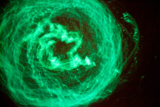 Grüne, wirbelnde Lichtmuster bilden vor einem dunklen Hintergrund eine kreisförmige, abstrakte Form.