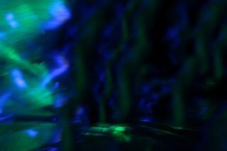 Abstraktes Bild mit verschwommenen Streifen aus blauem und grünem Licht, die vor einem dunklen Hintergrund ein dynamisches, fließendes Muster erzeugen.