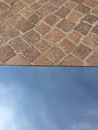 Auf einer Kopfsteinpflasteroberfläche liegt ein klarer Spiegel, der den Himmel darüber reflektiert.