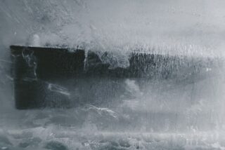 Ein großes Küchenmesser steckt in einem Eisblock, auf der Eisoberfläche sind Frost und Risse sichtbar.