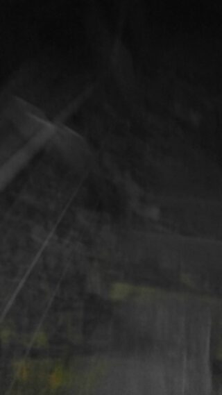 Verschwommenes, dunkles Bild mit schwachen Linien, Schatten und grünen und gelben Flecken, wodurch Details und Objekte nicht zu unterscheiden sind.