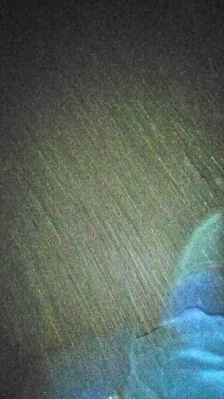 Eine Nachtszene mit starkem Regen und einer teilweise sichtbaren Person in einem blauen Regenmantel oder einer blauen Jacke in der unteren rechten Ecke.