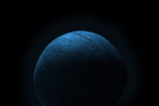 Eine schwach beleuchtete, blau getönte Kugel ist in der Mitte vor einem schwarzen Hintergrund abgebildet, wobei Licht ihre obere linke Oberfläche hervorhebt.