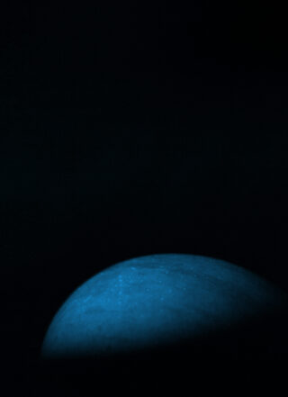 Vor einem dunklen Hintergrund ist eine schwach beleuchtete blaue Kugel teilweise sichtbar, die von unten beleuchtet wird und eine schattige und geheimnisvolle Atmosphäre schafft.