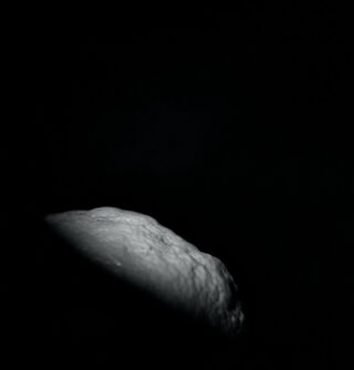 Eine schwach beleuchtete, strukturierte Oberfläche, möglicherweise eine Nahaufnahme einer Zitrone oder Zitrusfrucht, wird vor einem überwiegend dunklen Hintergrund gezeigt.