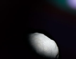 Eine Nahaufnahme einer teilweise beleuchteten Zitrone vor einem dunklen Hintergrund, wobei der Großteil des Bildes im Schatten liegt.