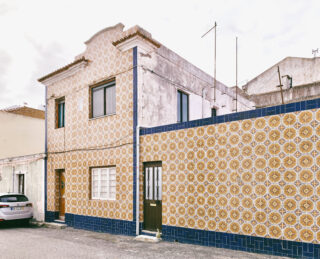 Ein zweistöckiges Gebäude mit dekorativen gelb-weiß gemusterten Fliesen an der Fassade, blauen Fliesenleisten und braunen Türen, gelegen in einer ruhigen Straße.