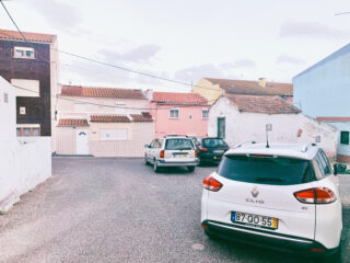 Drei geparkte Autos in einer ruhigen Wohnstraße mit pastellfarbenen Häusern und Ziegeldächern im Hintergrund.