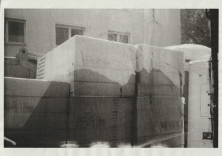 Ein Stapel großer, rechteckiger Schaumstoff-Dämmplatten ist im Freien an einer Gebäudewand angebracht, darüber sind zwei Fenster sichtbar.