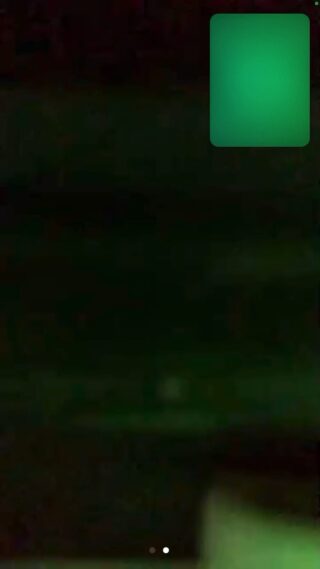 Ein dunkles, verschwommenes Bild mit einer grünen Überlagerung in der oberen rechten Ecke und zwei kleinen weißen Punkten in der Nähe der unteren Mitte.