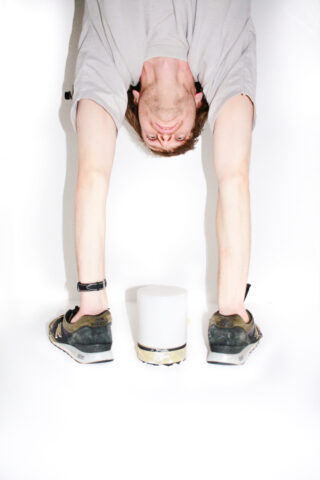 Eine Person in einem grauen Hemd steht kopfüber vor einem weißen Hintergrund und greift nach einem weißen zylindrischen Objekt zwischen ihren Händen.