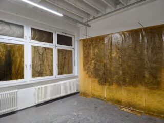 Raum mit großen Fenstern und Heizkörpern; Fenster und ein Teil der Wand sind mit lichtdurchlässigen, bernsteinfarbenen Kunststofffolien verkleidet.