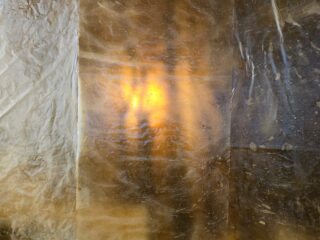 Eine durchscheinende, strukturierte Oberfläche mit einer warmen, gelb-orangen Lichtquelle, die von hinten durchscheint und diffuse Schatten und ein gesprenkeltes Erscheinungsbild erzeugt.