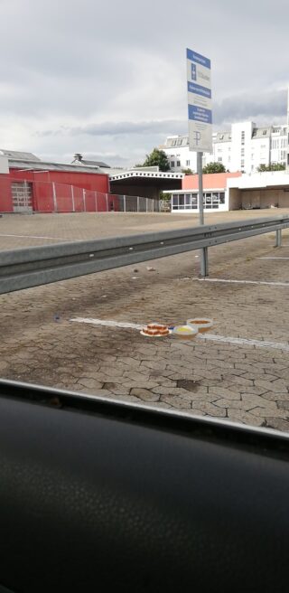 Ein verschütteter Kuchen liegt auf dem Bürgersteig in der Nähe eines Parkplatzes, im Hintergrund sind eine Straßensperre und ein Schild zu sehen.