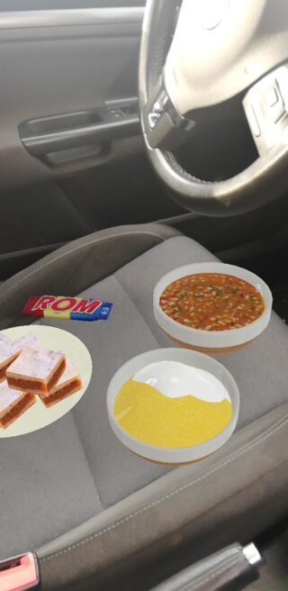 Ein Autositz mit einem Teller mit geschichteten Scheiben, einer Schüssel mit gelbem Getreide, einer Schüssel mit Eintopf und einem IROM-Energieriegel darauf.