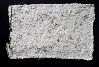 Ein rechteckiges Blatt raues, handgeschöpftes Papier mit sichtbaren Fasern und unebenen Kanten, auf schwarzem Hintergrund.