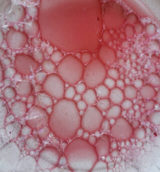 Nahaufnahme von rosa Seifenblasen, die auf einer hellen Oberfläche zusammengeballt sind.