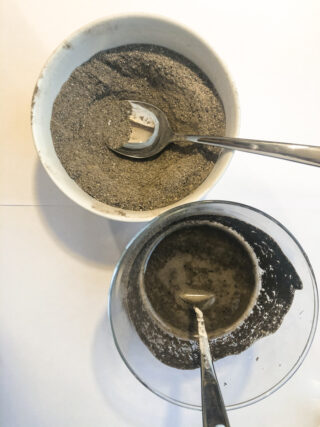 Zwei Schüsseln, eine weiße und eine durchsichtige, enthalten jeweils ein gräuliches Pulver und einen Metalllöffel; in der durchsichtigen Schüssel ist außerdem Flüssigkeit mit dem Pulver vermischt.