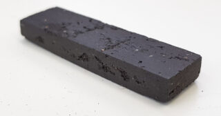 Ein rechteckiger, schwarzer, leicht rauer Massivblock, der auf einer weißen Oberfläche liegt.