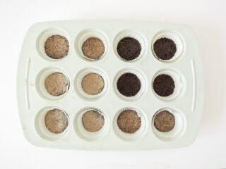 In eine weiße Muffinform passen zwölf Cupcake-Förmchen, die jeweils mit einem hellbraunen oder dunkelbraunen körnigen Pulver gefüllt sind.