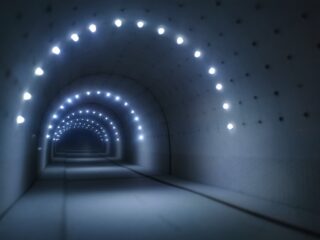 Ein schwach beleuchteter Tunnel mit Reihen kreisförmiger weißer Lichter entlang der gewölbten Decke, die ein Gefühl von Tiefe und Perspektive erzeugen.