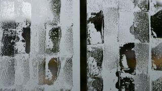 Glasoberfläche mit rechteckigen, abstrakten, in Spalten angeordneten weißen Farbmarkierungen, die den Blick hinter das Glas teilweise verdecken.