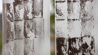 Glasoberfläche mit zwei Säulen aus quadratischen Flecken und Streifen in einem gitterartigen Muster, die möglicherweise durch Reinigen oder Wischen entstanden sind.