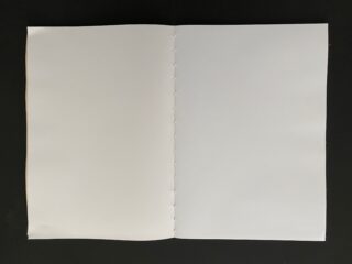 Ein offenes, leeres Buch mit weißen Seiten und sichtbarer Naht entlang des Buchrückens, auf einer schwarzen Oberfläche.
