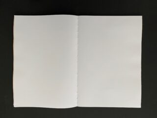 Ein offenes, leeres Buch mit weißen Seiten liegt flach auf einer dunklen Oberfläche.