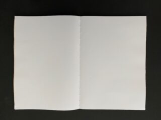 Ein offenes, leeres Notizbuch mit weißen Seiten liegt zentriert auf einer dunklen Oberfläche.