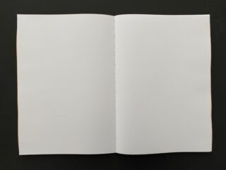 Ein offenes, leeres Notizbuch mit weißen Seiten liegt flach auf einer dunklen Oberfläche.
