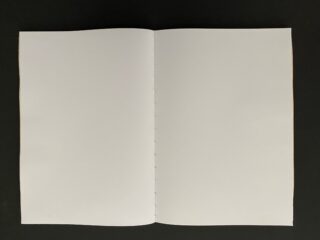 Ein offenes, leeres Buch mit weißen Seiten liegt flach auf einer dunklen Oberfläche und zeigt den Mittelrücken und die Nähte.