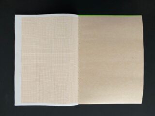 Ein offenes Notizbuch auf einer schwarzen Oberfläche, das eine linke Seite mit einem schwachen Gittermuster und eine leere braune rechte Seite zeigt.