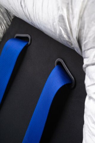 Eine Nahaufnahme von zwei blauen Bändern, die durch schwarze rechteckige Kunststoffschlaufen auf einer schwarzen Stoffoberfläche gefädelt sind, mit silbernem Isoliermaterial an der Oberseite.