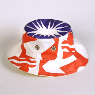 Ein Anglerhut mit einem kräftigen abstrakten Muster in Rot, Weiß und Blau und zwei Metallösen an der Seite, fotografiert vor einem einfarbigen Hintergrund.