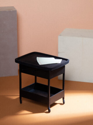 Auf einem schwarzen Rollwagen liegt ein einzelnes Blatt liniertes Papier vor einem Hintergrund mit hellorangen und beigen Wänden.