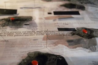 Eine Nahaufnahme einer gedruckten Seite mit deutschem Text, bedeckt mit durchscheinendem Material, dunklen Flecken und darauf platzierten roten Pillen.