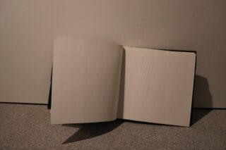 Ein offenes Buch mit leeren Seiten steht aufrecht vor einem schlichten Hintergrund auf einer strukturierten Oberfläche.