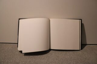 Ein offenes, leeres Buch liegt auf einer grauen Fläche vor einem neutralen Hintergrund.