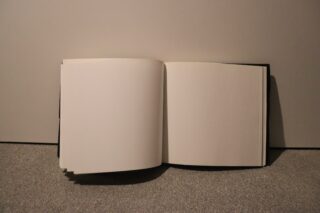 Ein offenes Buch mit leeren Seiten liegt auf einer strukturierten Oberfläche vor einem schlichten Hintergrund.