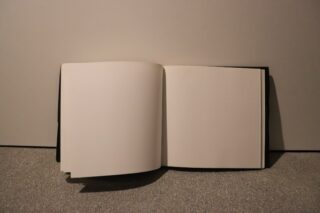 Ein offenes Buch mit leeren Seiten liegt auf einer strukturierten Oberfläche vor einem schlichten Hintergrund.
