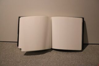 Ein offenes Buch mit leeren, weißen Seiten auf einer grauen Fläche vor einem schlichten Hintergrund.