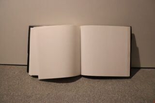 Ein offenes Buch mit leeren Seiten, das auf einer flachen, strukturierten Oberfläche vor einem schlichten Hintergrund liegt.