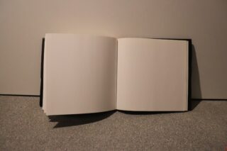Ein offenes Buch mit leeren Seiten liegt auf einer grauen Fläche vor einem schlichten Hintergrund.
